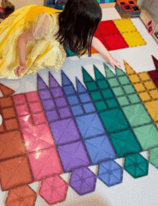 A child sorts magnetic tiles by shape and colour, carefully arranging them into organised groups creating a castle-like 2D pattern.