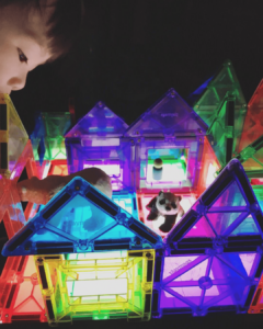  A young toddler using magnetic tiles to explore light and reflections in a light table, passes through transparent tiles, fostering curiosity about science and visual effects. 