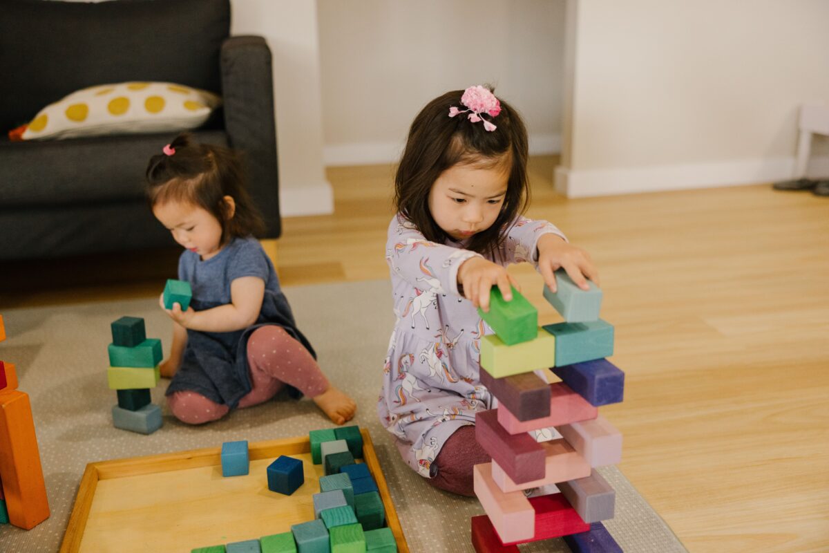 Two toddlers building structures using the open-ended toy Grimm's Large Stepped Pyramid block set