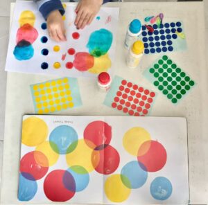 A toddler activity setup using recyclable cardboard, wooden pegs, and colorful dot stickers. Toddler match the colour on the pegs to the dot stickers on the corrugated cardboard.