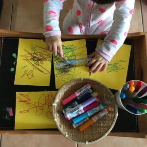 Toddler using blue markers to draw additional details on a previously created piece of artwork.