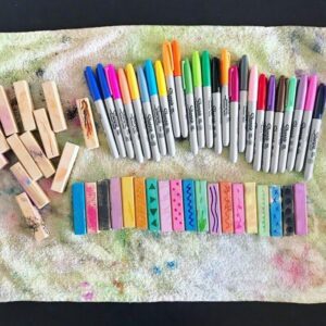 Painted wooden blocks set up as an invitation for toddlers to draw on. The blocks, adorned with vibrant colors, are arranged alongside markers, encouraging creative exploration and extending the art activity.