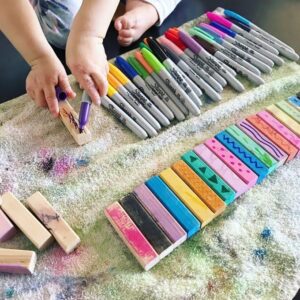 A toddler adding scribble details to a painted wooden block using a Sharpie marker