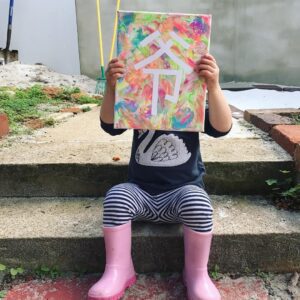 Toddler proudly displaying their washi tape painting masterpiece. The word on the masterpiece was dad, making a perfect gift for daddy. 