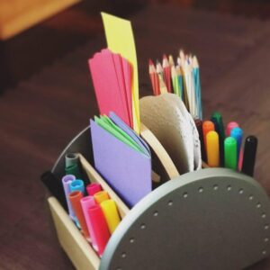 Art caddy filled with a variety of supplies: different colors and sizes of construction paper stacked neatly, along with washable markers and colored pencils arranged for easy access. The caddy is ready for creative projects and drawing activities.