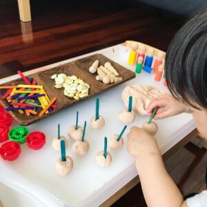 Toddler sticking popsicle sticks into playdough, placing them with focus and concentration, while working on their fine motor skills. 