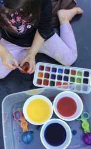 Materials set up for a colour exploration activity, featuring an ice tray for the child to explore, three primary colours in large bowls, and droppers for mixing and experimenting with the colours. 
