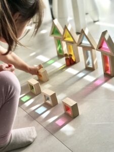 A preschooler arranging colorful blocks against a light source, creating colourful shadows on the surface
