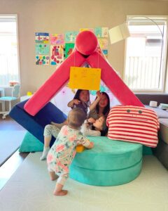 Siblings playing together inside a house they built using parts of a play couch, collaborating and enjoying their own cozy space.
